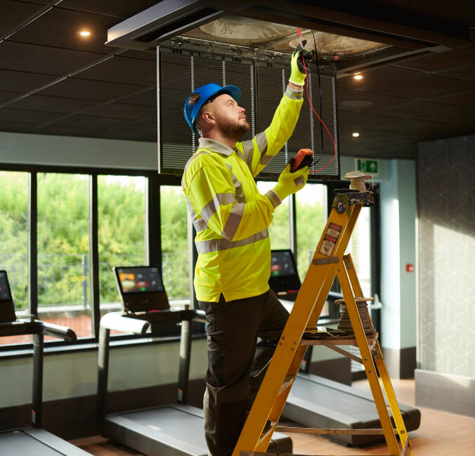 Man fixing wiring in the ceiling of a gym