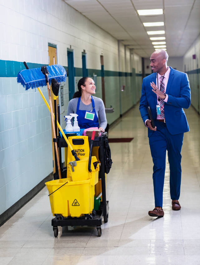 Cleaning staff pushing professional cleaning equipment cart in large facility