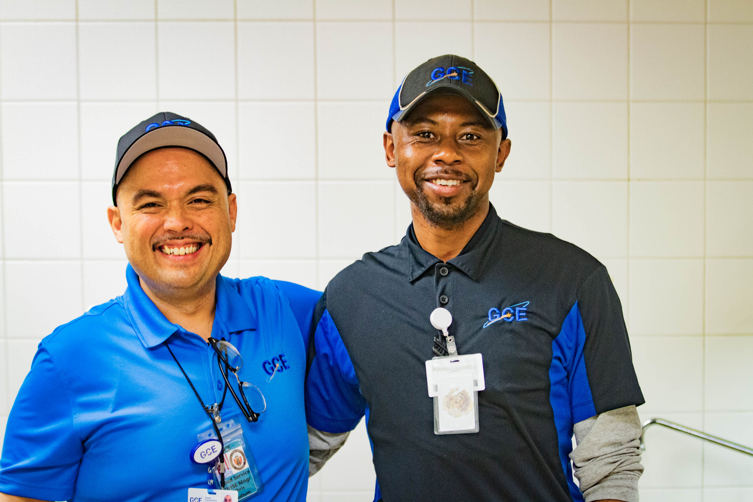 Two male coworkers standing side-by-side with an arm around their shoulders